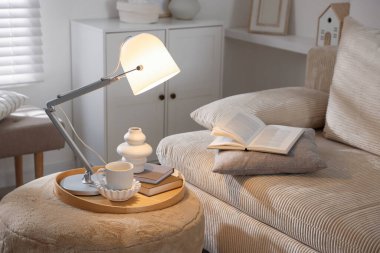 Şık lamba, vazo, kitaplar ve fincanlar kapalı koltuğun yanında.