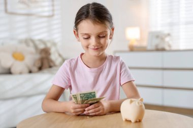Küçük kız cep harçlığı ve domuz kumbarası ile ahşap masada.