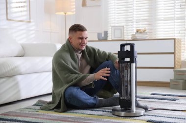 Evdeki elektrikli ısıtıcının yanındaki genç adam.