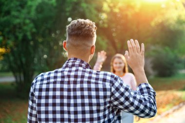 Bir adam parkta arkadaşına el sallıyor, seçici odaklanma.