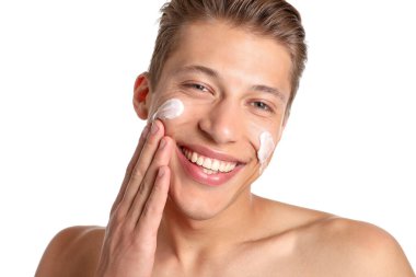 Beyaz arka planda yüzüne krem süren yakışıklı genç adam, yakın plan.