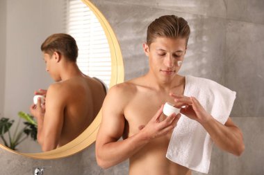 Banyoda yüz kremi dolu kavanozu olan yakışıklı bir genç.