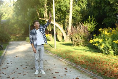 Mutlu genç adam parkta el sallıyor, mesaj için yer var.