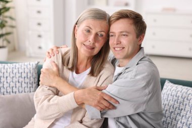 Mutlu oğul ve annesi evde kanepede kucaklaşıyorlar.