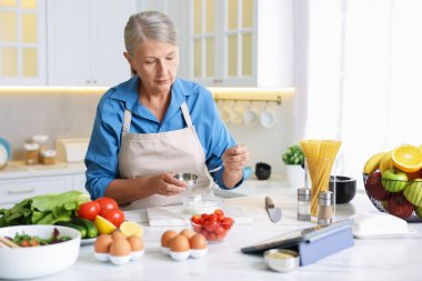 Üst düzey kadın mutfaktaki beyaz mermer masada yemek pişiriyor.