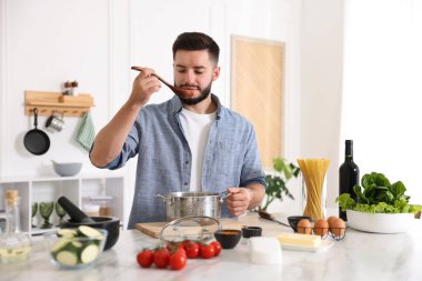 Genç adam mutfakta yemek yaptıktan sonra yemeği tadıyor.