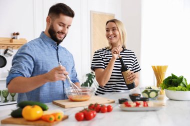 Gülümseyen kadın mutfakta kocasıyla yemek pişirirken şarap şişesini açıyor.