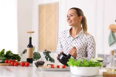 Mutfaktaki masada yemek yapan gülümseyen kadın.