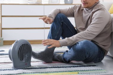 Evdeki elektrikli ısıtıcının yanındaki genç adam, yakın çekim.