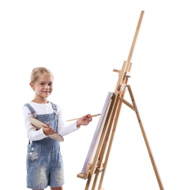 Meslek seçimi. Beyaz arka planda ressammış gibi davranan palet boyalı ve sehpanın yanındaki fırçalı küçük kız.