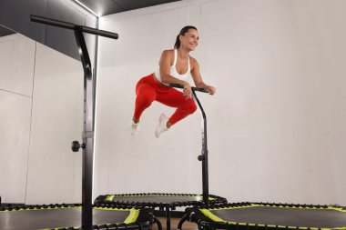 Spor salonunda trambolinde zıplayan gülümseyen kadın, düşük açı.