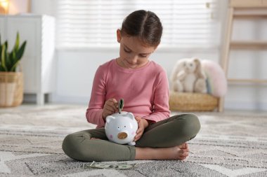 Küçük kız evdeki domuz kumbarasına cep harçlığı koyuyor.