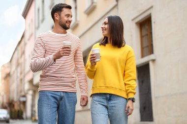Paket kahve. Kağıt bardaklı bir çift şehir caddesinde yürüyor, düşük açılı.