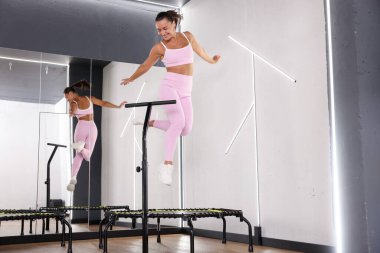 Spor salonundaki aynanın yanında trambolinde zıplayan gülümseyen kadın, düşük açılı görüş.