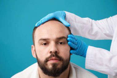 Kellik sorunu. Tıbbi eldivenli doktor açık mavi arka planda hastanın kafasını muayene ediyor, yakın plan.