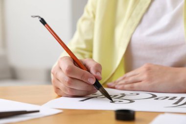 Kaligrafi. Fırça darbeleriyle yazı yazan kadın. Kapalı alandaki masa kâğıdının ucuna yakın plan.