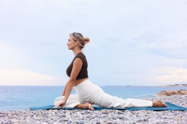 Plajda yoga yapan genç bir kadın.