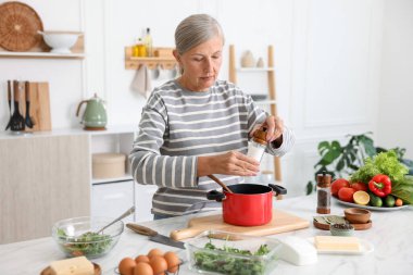 Üst düzey kadın mutfaktaki beyaz mermer masada yemek pişiriyor.