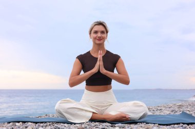 Plajda yoga yapan genç bir kadın.