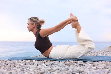 Plajda yoga yapan genç bir kadın.