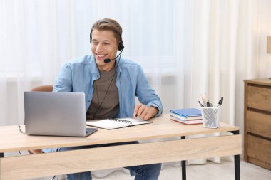 Kulaklıklı bir adam çevrimiçi sınavı içerideki masada laptopla geçiyor.