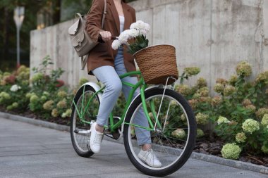 Şehir caddesinde elinde çiçeklerle bisiklet süren bir kadın, yakın plan.