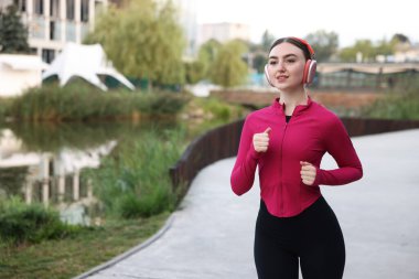 Nehir kenarında koşan kulaklıklı, gülümseyen bir kadın. Metin için boşluk