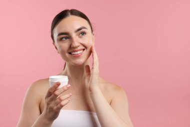 Güzel bir kadın pembe arka planda yüzüne krem sürüyor. Metin için boşluk