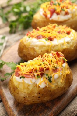 Ekşi kremalı fırında patates, yeşil soğan, ahşap masada peynir ve pastırma, yakın plan.