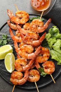 Lezzetli ızgara karidesli şişler, limon dilimleri, maydanoz, marul ve sos gri masada, üst manzara. Lezzetli deniz ürünleri yemeği.