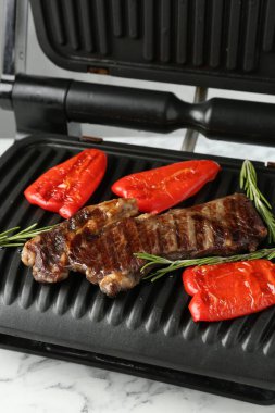 Elektrikli ızgara biftek, dolmalık biber ve biberiye beyaz mermer masada, yakın plan.