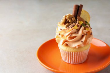 Delicious cupcake with color cream, nuts, cookie and cinnamon on grey table, closeup. Space for text