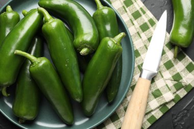 Fresh jalapeno peppers and knife on black table, above view