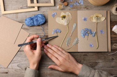 Ahşap masa, üst manzara, kuru çiçekleri deftere koyan kadın.