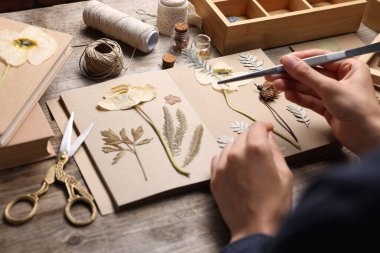 Ahşap masadaki kuru çiçekleri deftere koyan kadın, yakın plan.