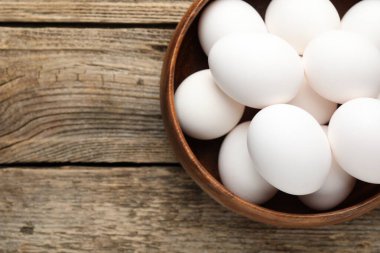 Fresh chicken eggs in bowl on wooden table, top view. Space for text