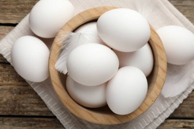 Raw chicken eggs and feathers on wooden table, top view