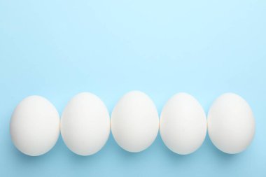 Fresh chicken eggs on light blue background, top view. Space for text