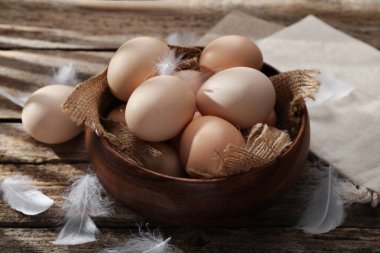 Tabakta çiğ tavuk yumurtası ve ahşap masada tüyler, yakın plan.