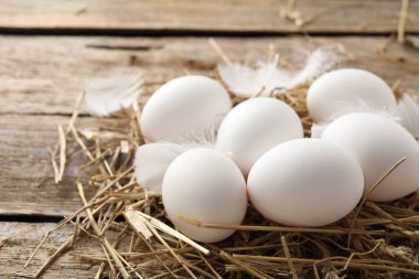 Raw chicken eggs, feathers and straw on wooden table, closeup