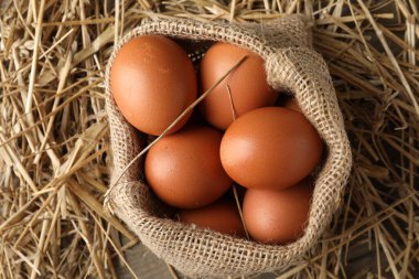 Raw chicken eggs in burlap sack and straw on table, top view
