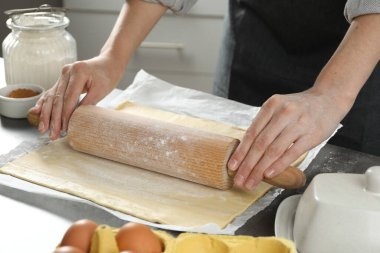 Elmalı turta yapıyorum. Mutfaktaki gri masada merdaneyle hamuru şekillendiren kadın, yakın plan.
