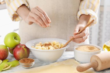 Elmalı turta yapıyorum. Mutfaktaki beyaz mermer masada meyveli kaseye tarçın tozu koyan kadın, yakın plan.