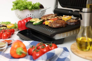 Electric grill with tasty meat and vegetables on table, closeup