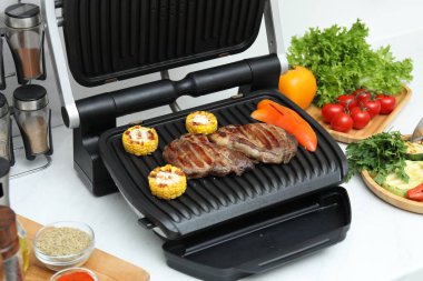 Beyaz tezgahta lezzetli et, sebze ve baharatla elektrikli ızgara.