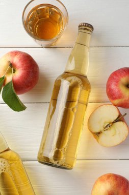 Cam şişelerde nefis elma şarabı ve beyaz ahşap masada elmalar.