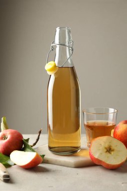 Şişede nefis elma şarabı, cam ve elmalar gri masada, arka planda ışığa karşı.