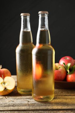 Cam şişelerde nefis elma şarabı ve ahşap masada koyu gri arka planda elmalar, yakın plan