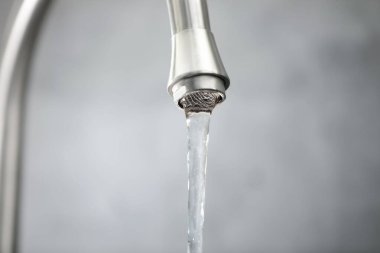 Su kavramını sakla. Gri arkaplandaki musluktan akan su akışı, yakın plan