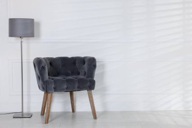 Stylish lamp and comfortable armchair near white wall indoors. Space for text